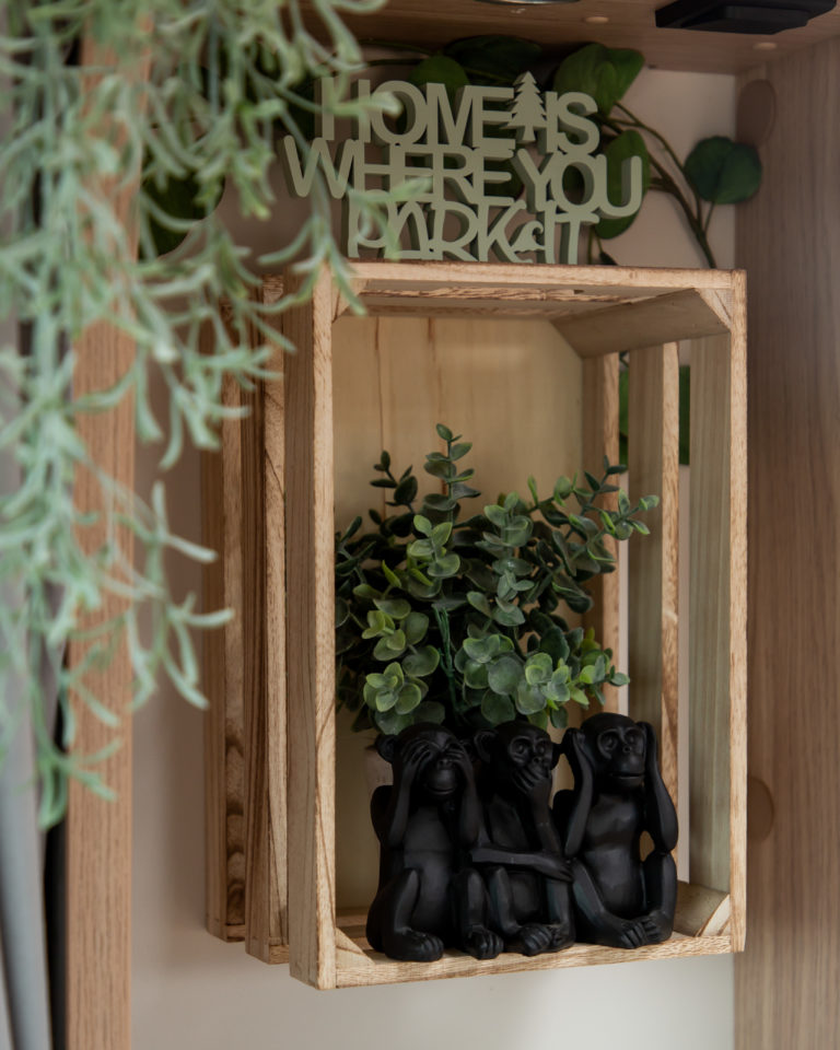 An der Wand hängende Holzkiste mit Kunstpflanzen und Affenfiguren als Wohnmobil Deko Inspiration